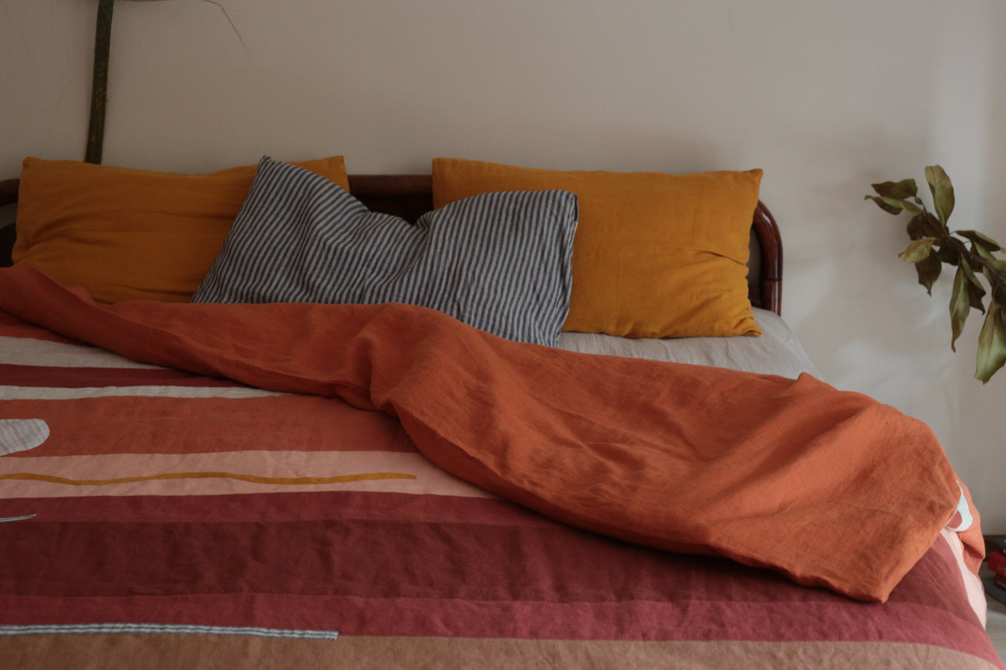 Bed with orange and gray pillows and a striped blanket in a room.