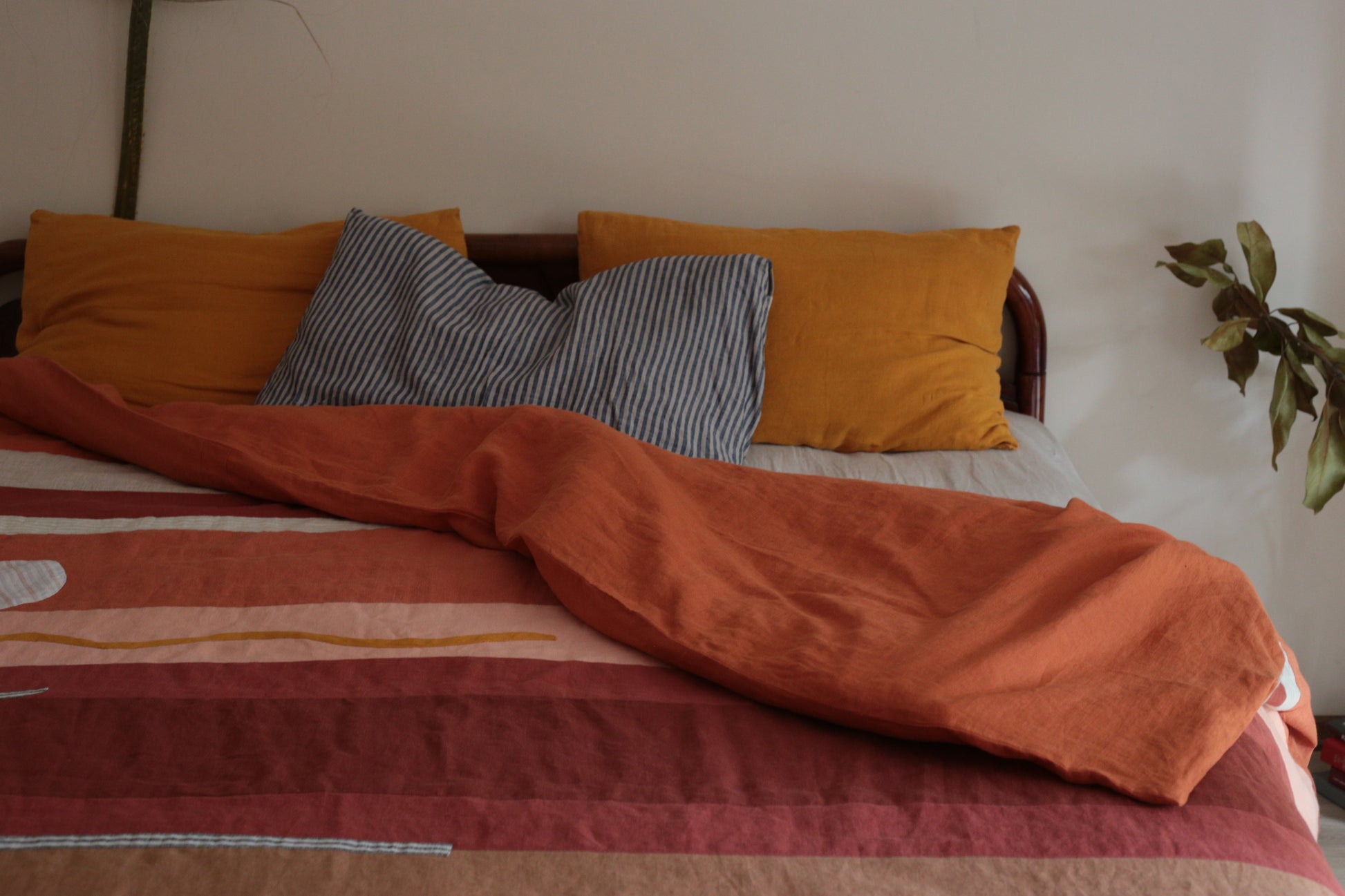 Bed with orange and gray pillows and a striped blanket in a room.